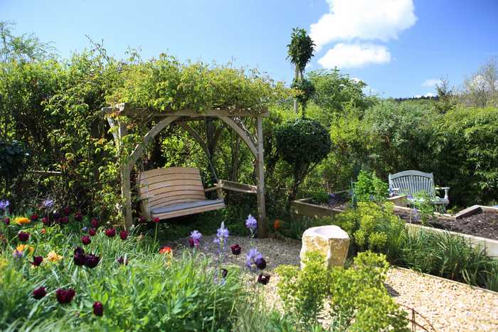Pergola and garden swing on gravel with flowers