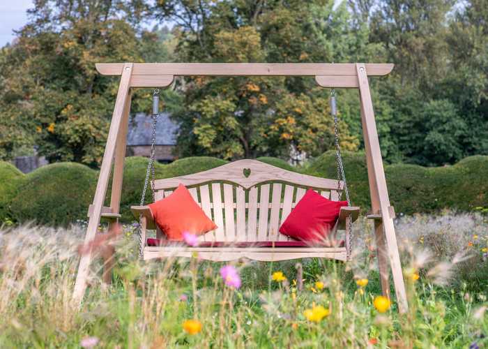 Wooden oak swing seat with red cushions set amongst wildflowers