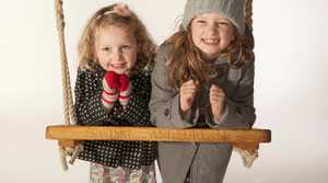 Two children smiling whilst leaning on personalised rope swing