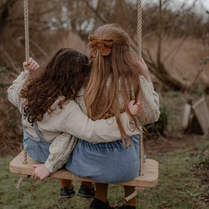 sisters swinging on a high quality swing seat hanging from a garden tree