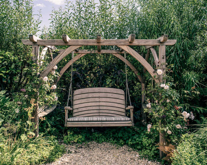 A wooden swing bench surrounded by lush greenery and flowering plants.