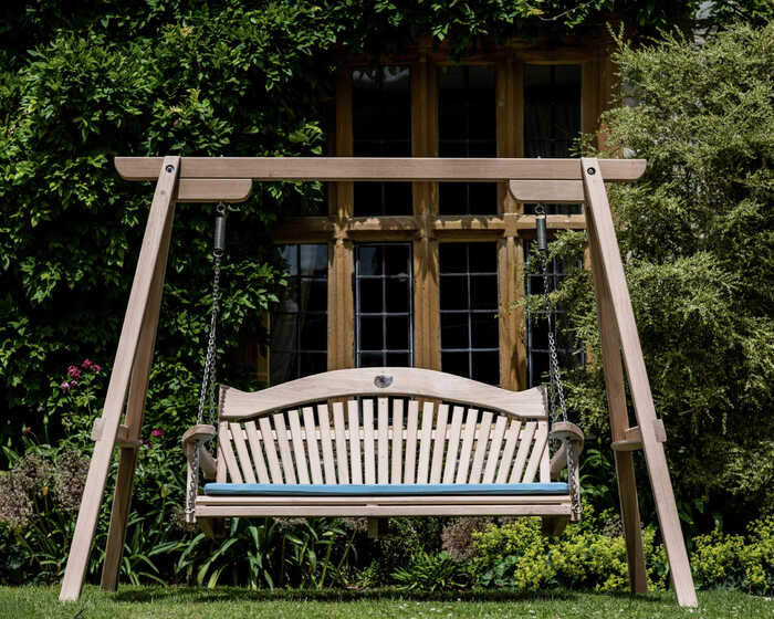 Wooden swing bench in a garden, surrounded by greenery and a house in the background.