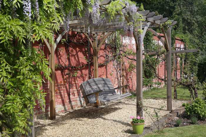 A swinging bench hanging from pergola, shaded with wisteria
