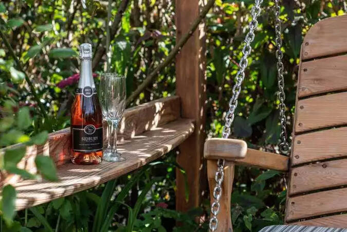 bottle-of-sparkling-rose-and-champagne-flute-on-swing-seat-armrest-1.webp