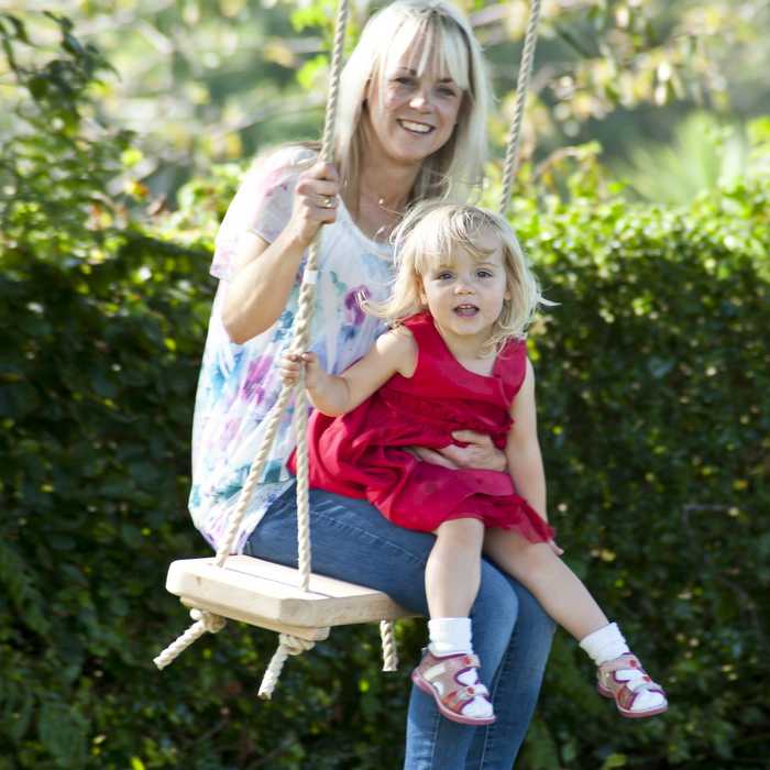 Mother and daughter swinging on a high quality swing seat hanging from a garden tree