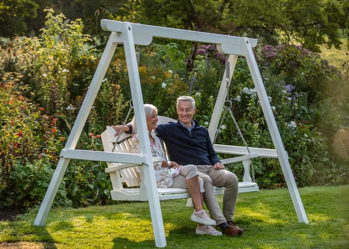 A couple smiling and laughing on a swinging seat in a garden