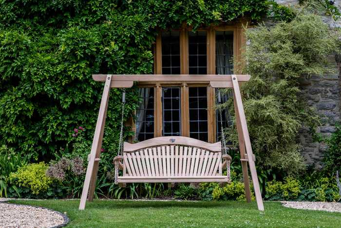 3 seater oak swing seat in front of building set on garden
