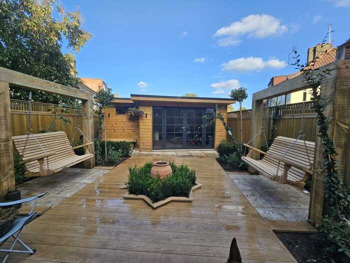 Two pergola arches with swing seats hanging in front of garden building - Designed by Lizzie Taylor