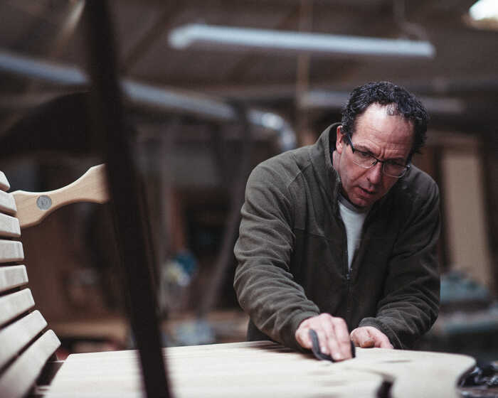 A man sanding a wooden chair in a workshop, focused on his work.