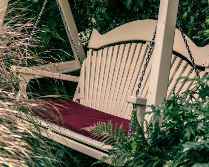 A cream-colored swing bench surrounded by white flowers and green foliage.