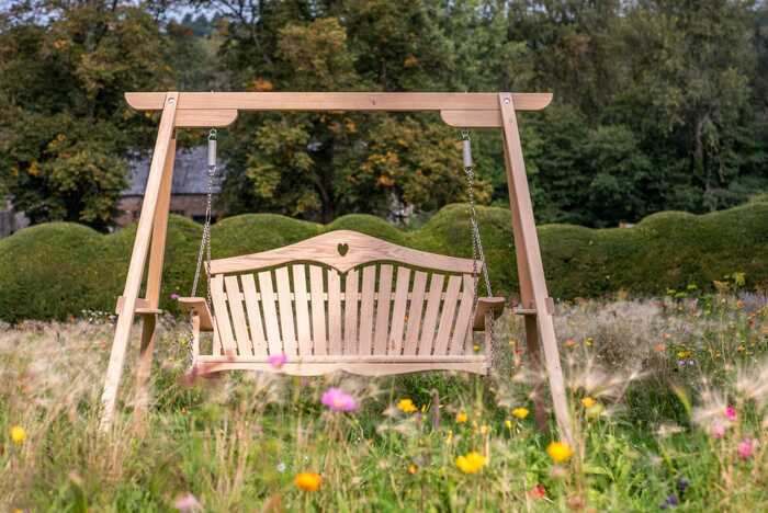 A wooden swing seat amongst wildflowers, with a heart back design 